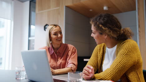 Two-young-adult-women-having-a-discussion-at-an-informal-meeting-in-an-office,-close-up