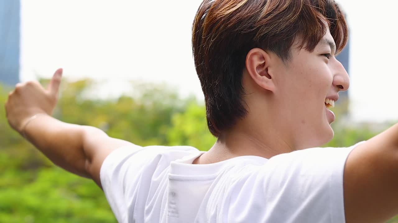 白いTシャツを着た、腕を大きく広げて屋外で喜ぶ陽気な若いタイ人男性