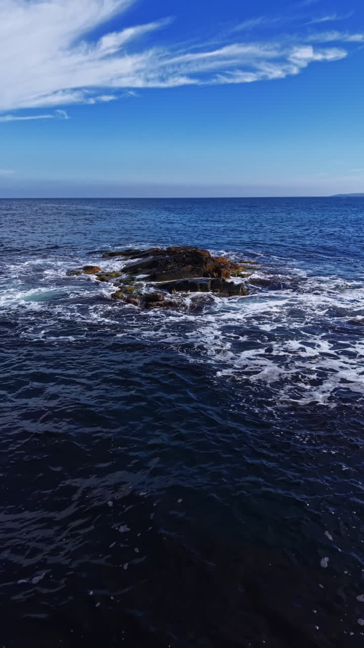 Onde maestose si infrangono contro uno sperone roccioso sotto un cielo azzurro brillante in riva al mare.