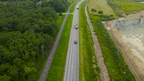 aerial drone footage descending and flying lower above a rural countryside highway where cars and vehicles are driving at a fast speed during summer day. a large limestone quarry next to the road