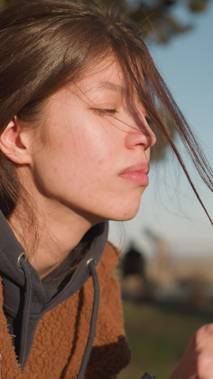 un primer plano de una chica con un abrigo marrón, mirando profundamente triste y ansiosa mientras tira de un hilo de su cabello. su expresión transmite una sensación de angustia y contemplación