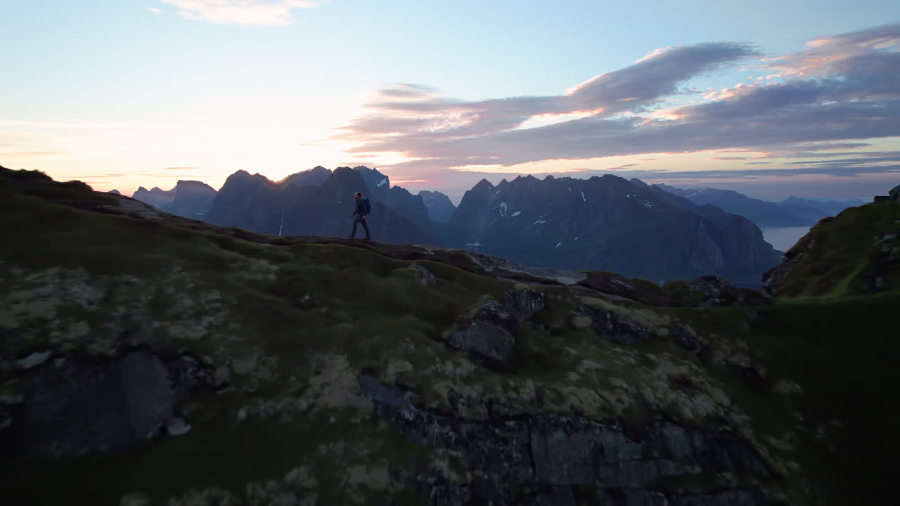 toma aérea hacia atrás de un dron que pasa por un excursionista en la famosa montaña reinebringen en lofoten
