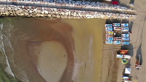 Aerial-top-down-shot-flying-an-empty-beach-and-a-breakwater-in-Caorle,-Italy-at-sunrise