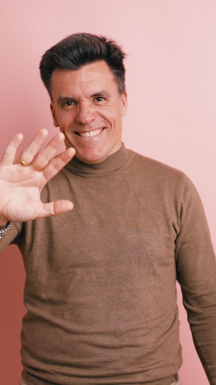 Uomo felice che saluta con la mano e sorride su sfondo rosa
