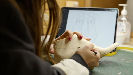 female craftsperson drawing creative design onto shoe last from template on digital ipad tablet