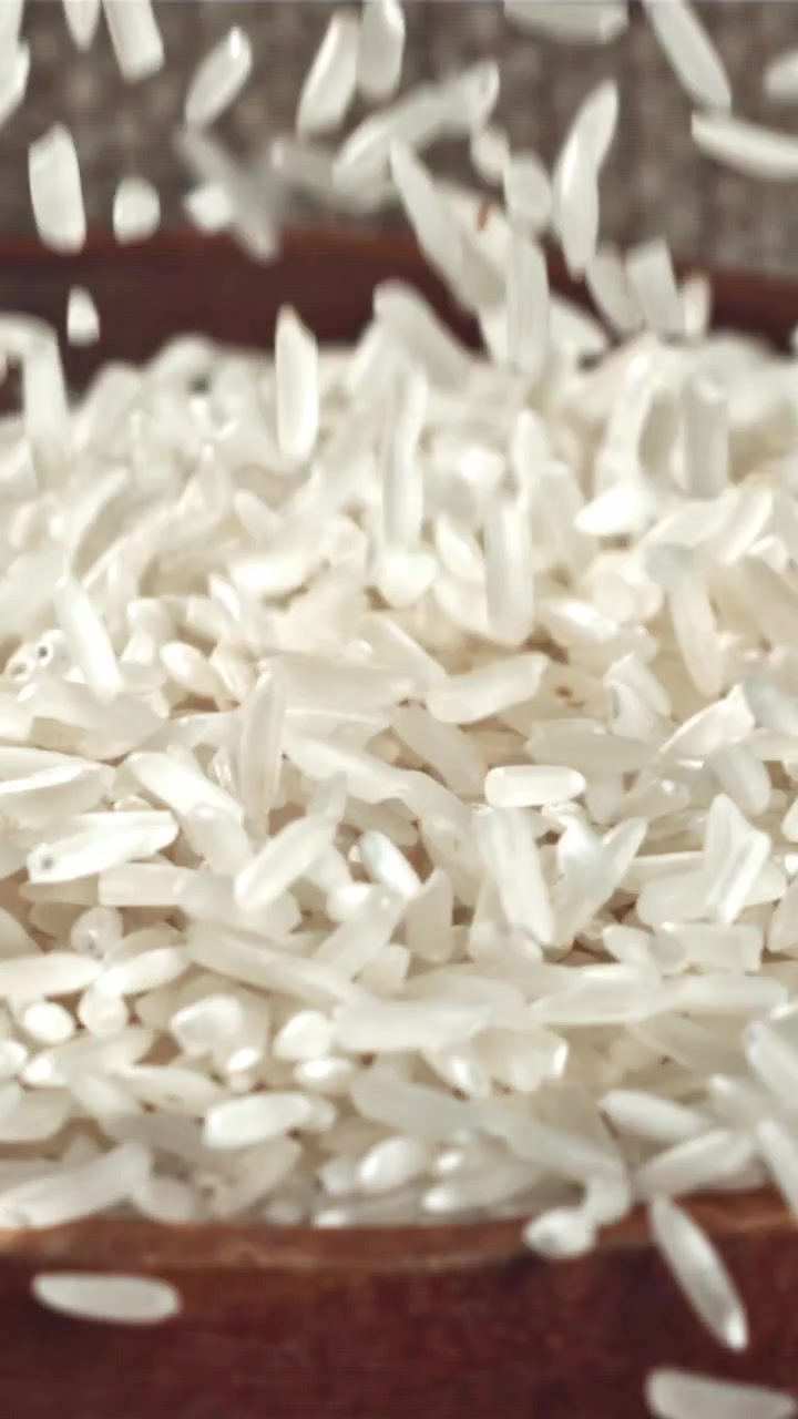 Chicchi di riso bianco che cadono in una ciotola di legno al rallentatore