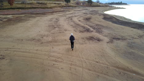 backview of a tourist walking on sandy coastline of lake jindabyne, new south wales, australia