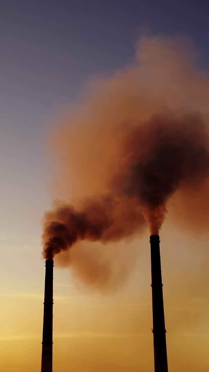 Orange smoke from pipes at sunset. Dirty emissions in the air on the evening sky background. Ecology pollution. Vertical video