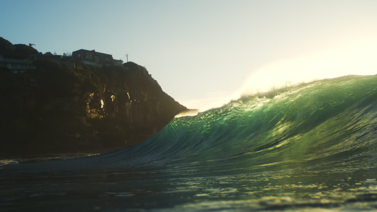 Slow motion backlit wave crashes along rocky golden coastline