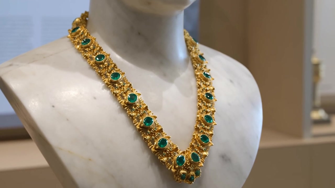 Telecamera che si allontana dopo una ripresa che rivela una collana d'oro con gemme verdi su un busto di marmo al museo.