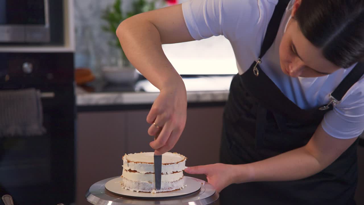 女性がキッチンで白いフロスティングを使ってレイヤーケーキをデコレーションしている