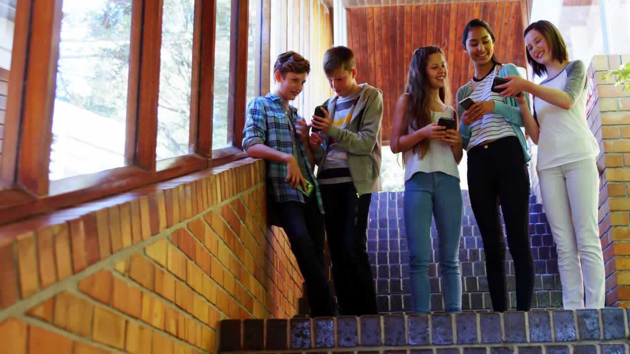 grupo de amigos de escola sorridentes usando telefone celular no corredor