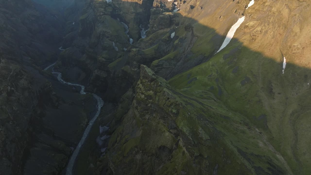 дронный снимок глубокого каньона в исландии, демонстрирующий крутые скалы, извилистую реку и неровную местность с пятнами снега