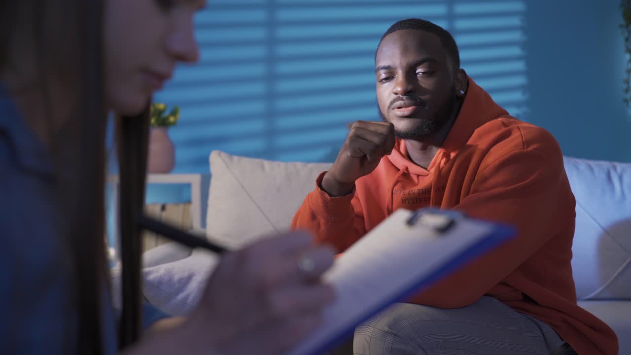 Psychologist taking notes during therapy session with upset black man. Mental and nervous diseases.