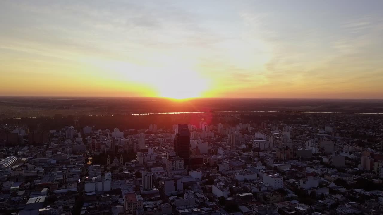 toma aérea del amanecer en una ciudad, mientras el sol sale por detrás de un edificio en un cielo lleno de colores y nubes