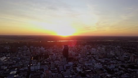 Toma-Aérea-Del-Amanecer-En-Una-Ciudad,-Mientras-El-Sol-Sale-Por-Detrás-De-Un-Edificio-En-Un-Cielo-Lleno-De-Colores-Y-Nubes