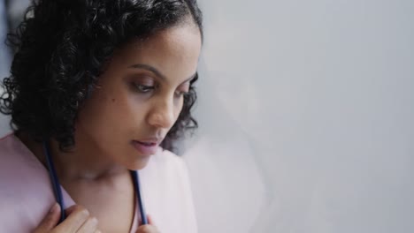 stressed biracial female nurse leaning on wall in hospital in slow motion