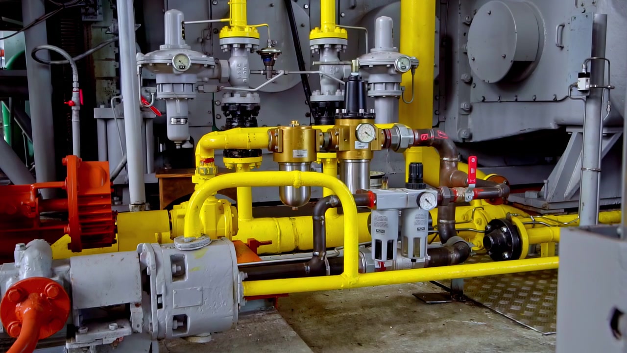 Attrezzature industriali complesse con tubazioni gialle, valvole e manometri in una fabbrica
