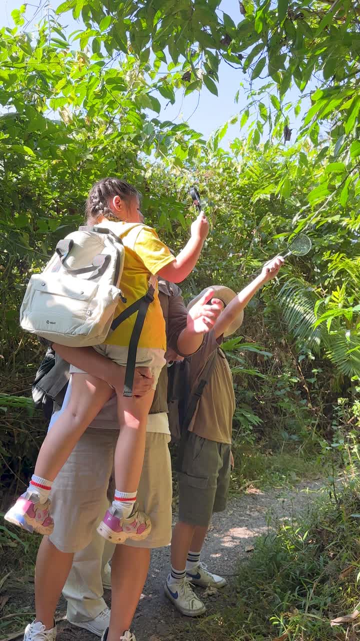 Young Asian children use magnifying glasses to explore lush jungle foliage under bright natural sunlight