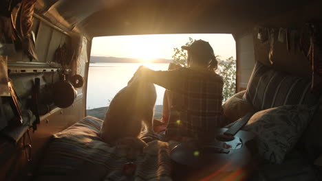 Mujer-Viendo-La-Puesta-De-Sol-Sobre-El-Lago-Desde-Una-Camioneta-Y-Un-Perro-Acariciador