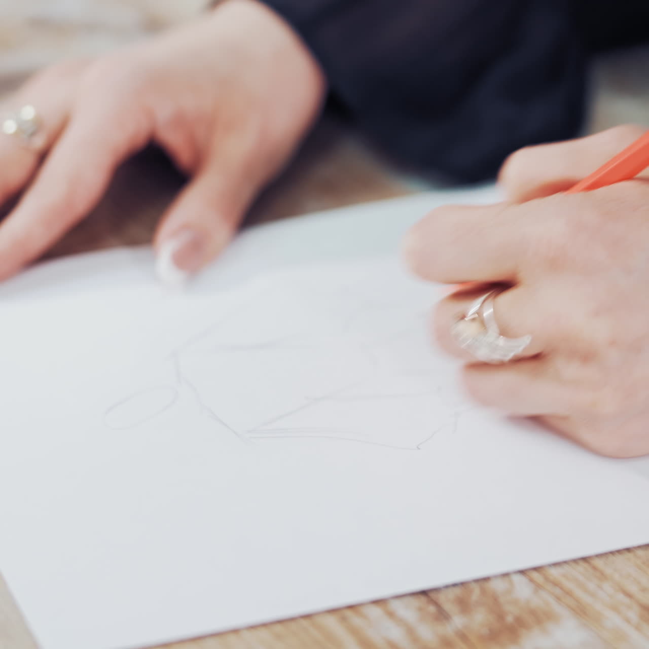 Female's hands drawing sketches of clothes on paper in her workplace. Clothes designer or tailor sketching with a pencil on a table.