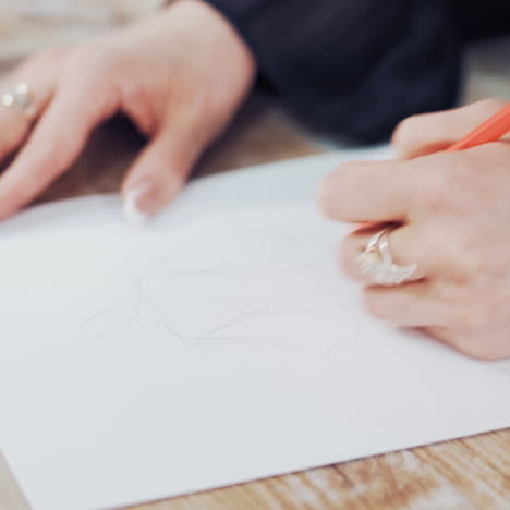 female's hands drawing sketches of clothes on paper in her workplace. clothes designer or tailor sketching with a pencil on a table.