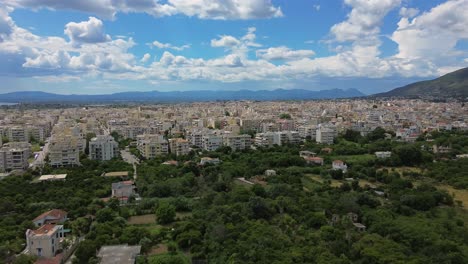 aerial panoramic view of kalamata city, spring day, with beautiful white cloud formations on blue sky, green olive orchards on foreground, left pan 4k shot