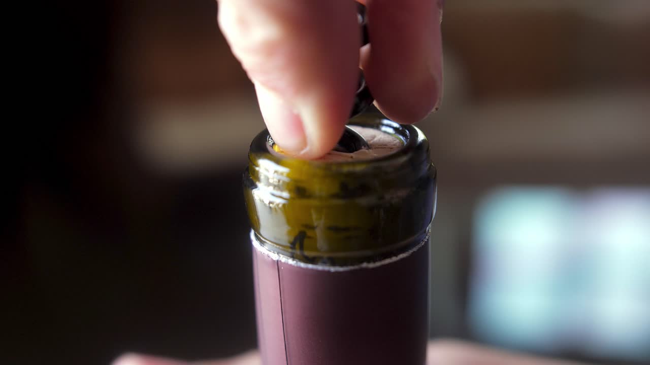 close-up shot of a corkscrew being inserted into a wine bottle's cork, capturing the moment of opening with hands holding the bottle steady.