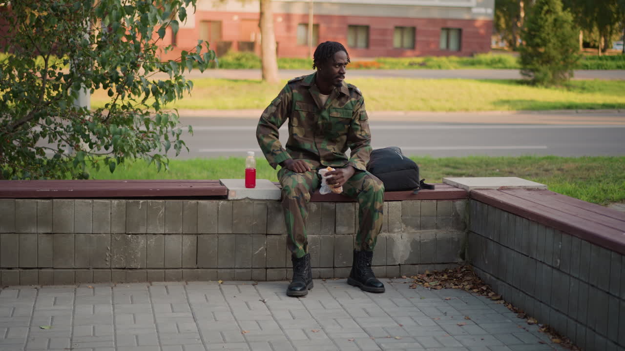 Black Soldier Resting On Bench, Sipping Coffee And Checking Phone In Suburban Park, Camouflage Uniform With Backpack At Side, Daytime Pause, Veteran Fatigue Mixed With Alertness, Field Medic Gesture