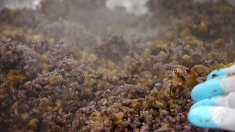 Pork-fried-with-soy-sauce-being-placed-into-a-large-bowl-of-steaming-hot-organic-purple-rice-then-mixed-together-by-hand