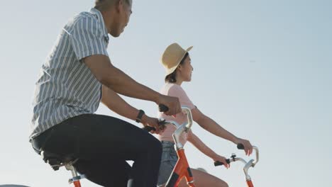 feliz pareja biracial montando bicicletas en el paseo marítimo, en cámara lenta