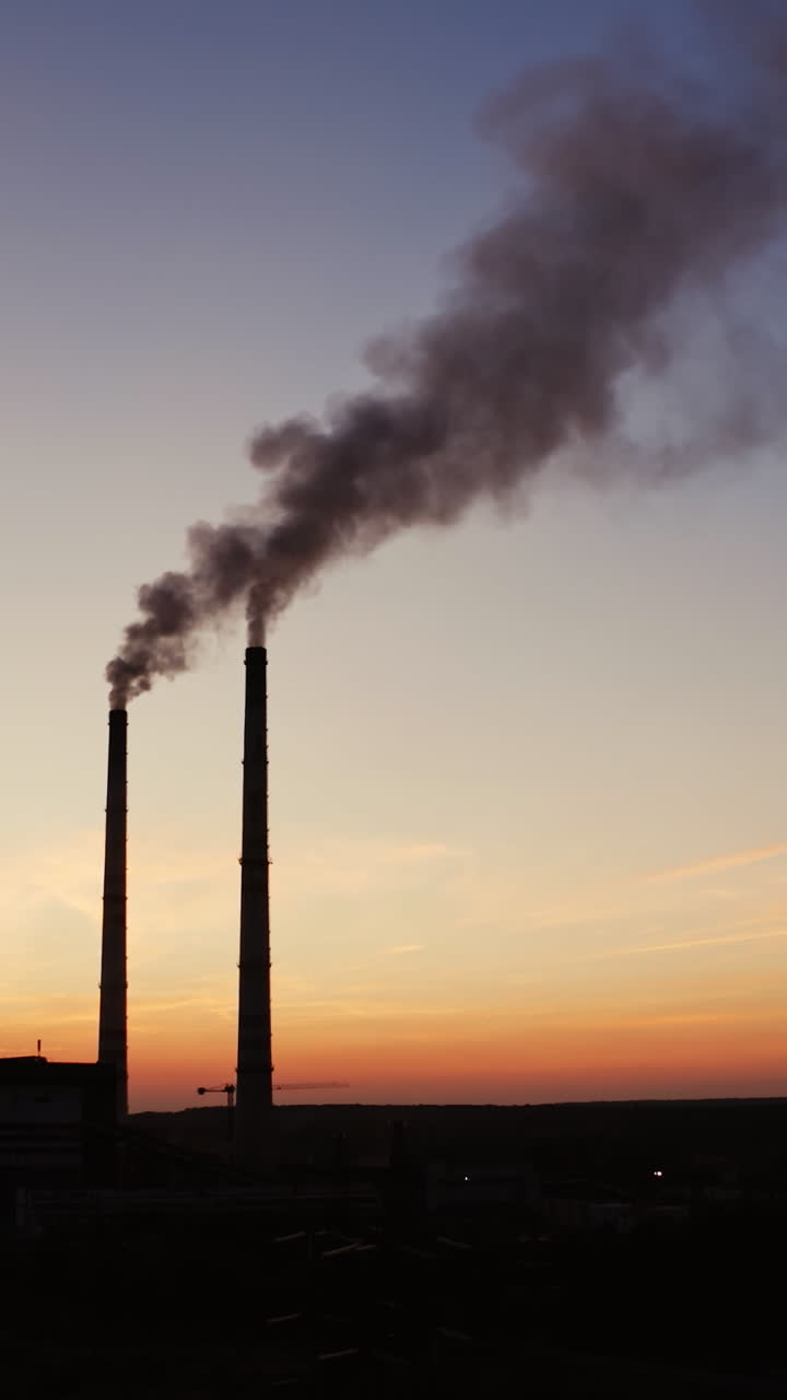Dark background of plant with industrial pipes. Smokestacks of the plant against the background of an orange sunset. Bad ecological situation. Air pollution. Vertical video