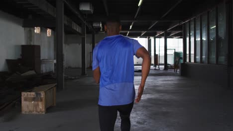 hombre afroamericano vestido con ropa deportiva corriendo a través de un edificio urbano vacío