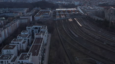 Aerial-view-of-a-passenger-train-passing-by-trees-in-Berlin,-Germany-surrounded-by-residential-house-during-an-early-morning