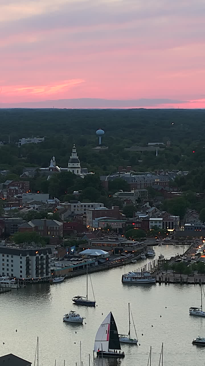 Marylands hovedstad, Annapolis. En fredfyldt havn strækker sig nedenfor, mens sejlbåde driver på roligt vand, og byen lyser blidt op under en pastel-solnedgangshimmel - Lodret billede