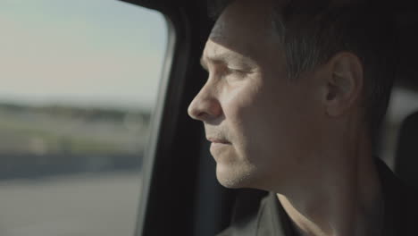 un hombre de mediana edad con una mirada preocupada en su rostro mira el camino por delante y luego se vuelve para mirar por la ventana del lado del pasajero mientras el auto vuela por la carretera