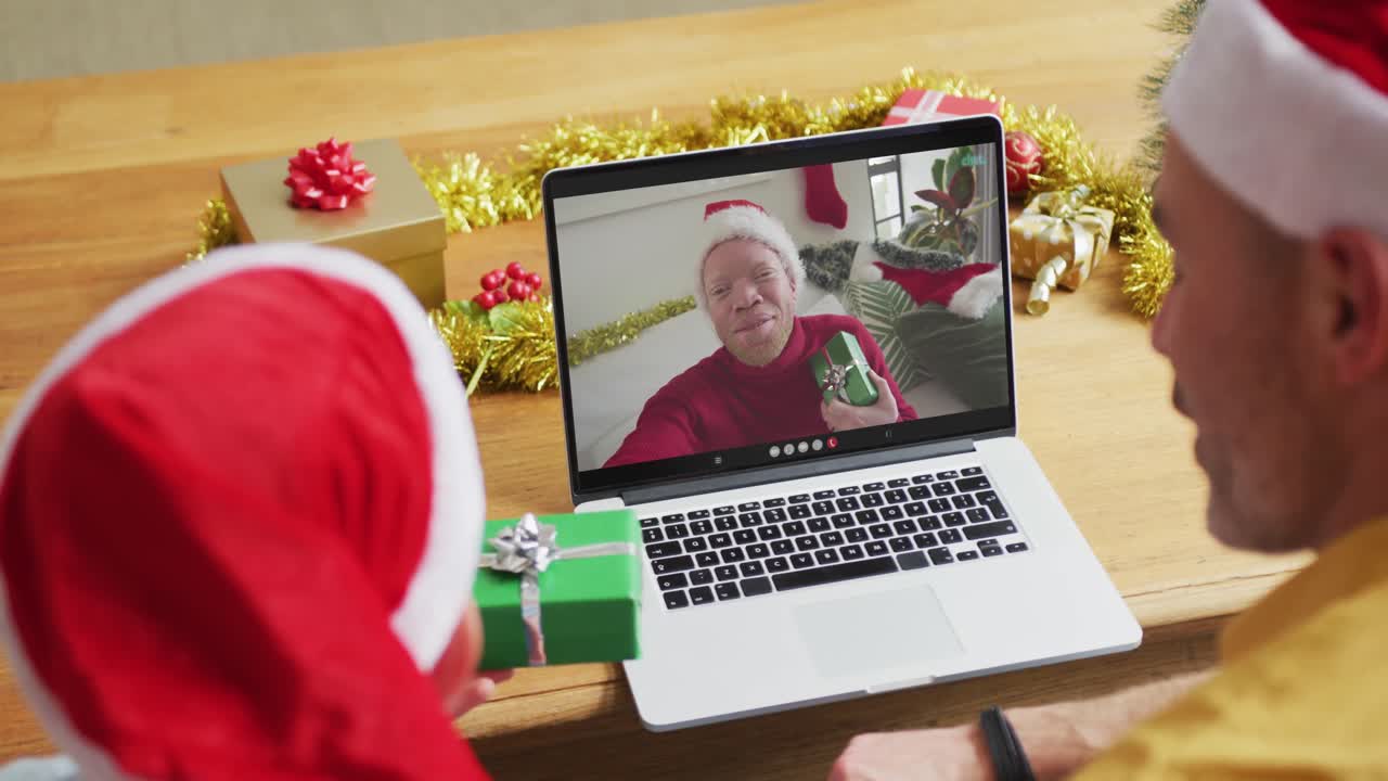 padre caucásico con su hijo usando una computadora portátil para una videollamada de navidad, con un amigo sonriente en la pantalla
