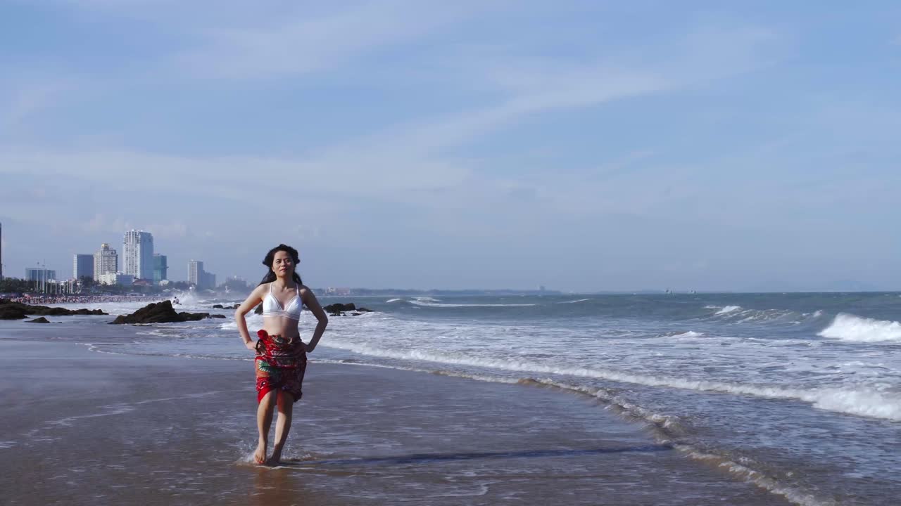 joven mujer asiática camina en la playa en vietnam con el horizonte de la ciudad en segundo plano