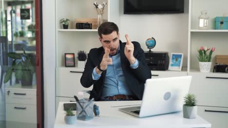 The-handsome-young-man-in-a-jacket-is-sitting-at-a-desk-in-the-office,-imagining-that-he-has-guns-in-his-hands-and-he's-shooting-with-them