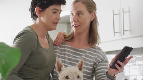 pareja de lesbianas caucásicas con su perro hablando en videollamada en el teléfono inteligente en casa