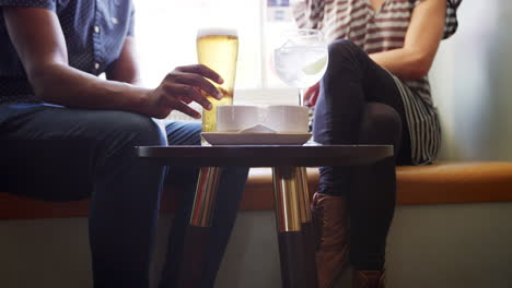 sección media de cerca de la pareja en conversación, sentado con bebidas en un asiento de la ventana en un pub, cámara lenta