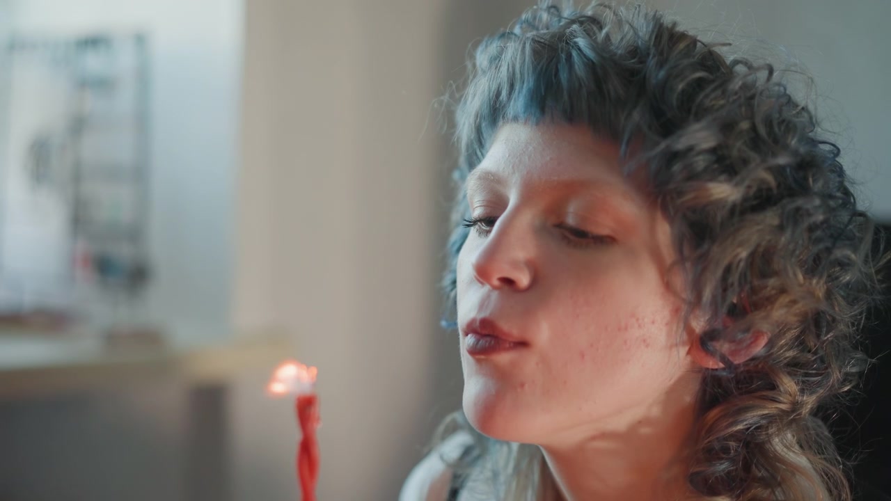 Mulher soprando vela durante ritual de adivinhação, clarividente moderna faz uma leitura de sorte íntima em apartamento aconchegante com cabelo cacheado emoldurando o rosto focado, chama suave e fumaça ondulando, cera pingando