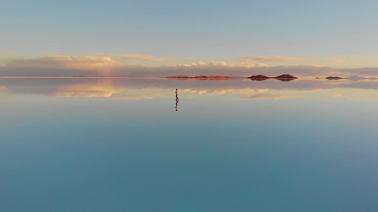 Aerial of a lone figure standing on the mirrored reflection of the world's largest salt flat in the Uyuni Salt Flats , Bolivia