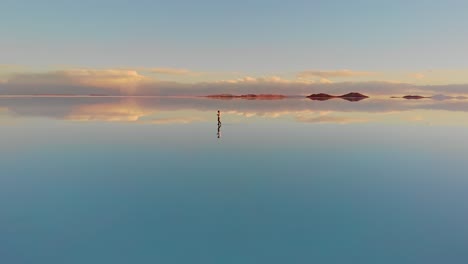 aerial of a lone figure standing on the mirrored reflection of the world's largest salt flat in the uyuni salt flats , bolivia