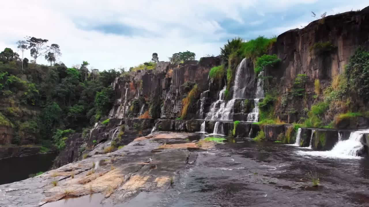Scenic aerial view of a stunning multi-tiered waterfall cascading over rocky cliffs, nestled in the lush Vietnamese landscape.