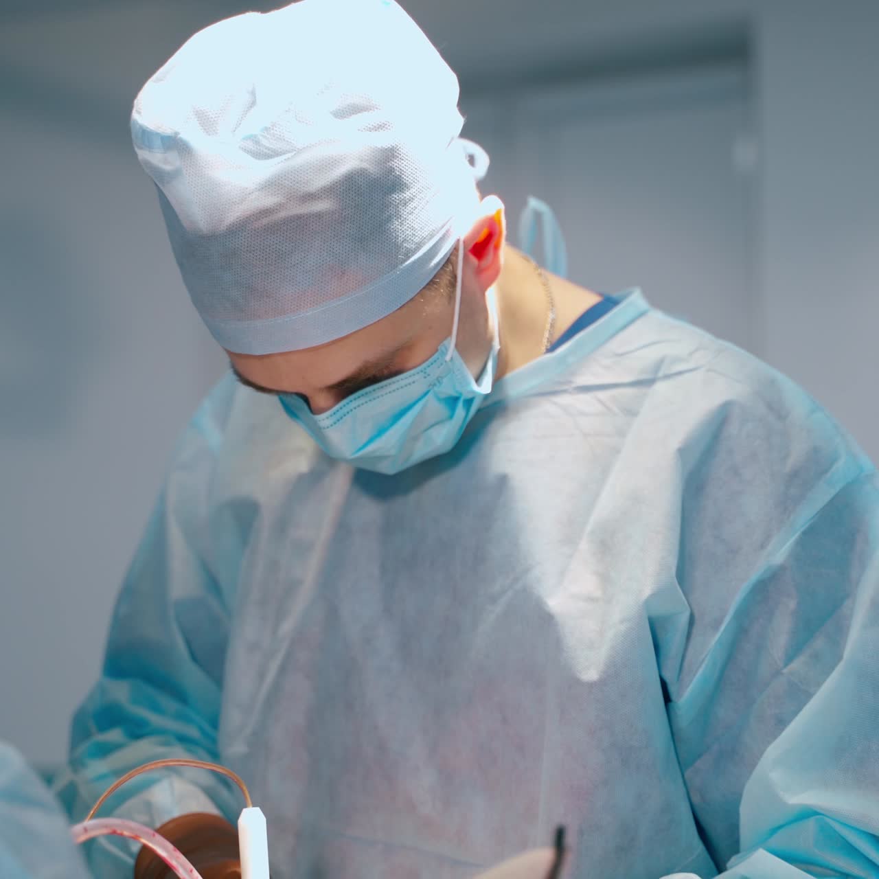 Portrait of a doctor during operation process. Professional surgeon in medical uniform performing a surgery with surgical tools. Nurse helps the doctor in clinic.