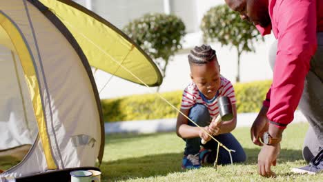happy african american father and son pitching tent together in sunny garden, in slow motion