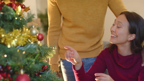 Happy-diverse-couple-decorating-christmas-tree-at-home,-slow-motion