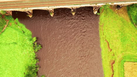 aerial top down view of a river running under a railway viaduct in the english countryside, bright daylight