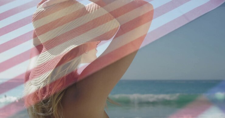 Transparent flag overlay waving across shoreline opening woman adjusting straw hat to shield eyes